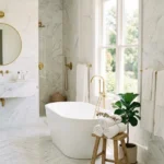 Bright white bathroom with marble tiles, gold fixtures, and natural light creating a clean and elegant spa-like look
