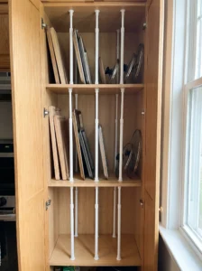 Tension rods creating organized storage slots for pantry trays and lids