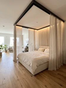 Open-plan bedroom with linen curtains defining the bed zone without walls