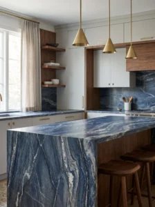 Deep blue quartzite kitchen island with dramatic white and silver veins, pale cabinets, and brass hardware.