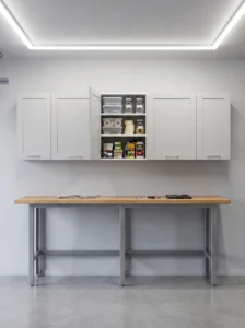 White ENHET-style wall cabinets above a garage workbench, concealing organized hardware, tape, and car-care supplies.