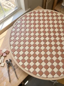 Square ceramic mosaic tiles turned diagonally to create an ivory and terracotta diamond pattern on a framed tabletop.