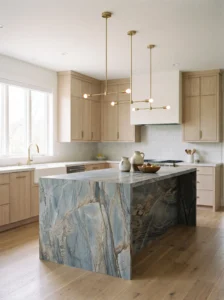 Blue-gray quartzite kitchen island with natural brown streaks, cream cabinets, and understated pendant lighting.