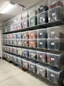 Clear lidded SAMLA-style storage bins stacked on garage shelves with organized seasonal decorations and holiday lights.
