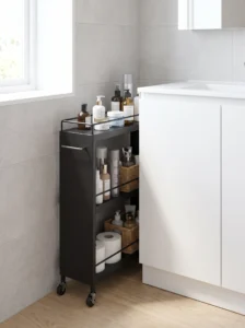 Slim three-tier rolling bathroom cart tucked beside a vanity with organized toiletries, hair products, and spare toilet paper.