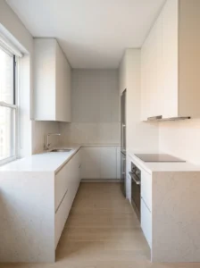 Compact U-shaped kitchen with a continuous pale quartz countertop, white cabinets, and an uncluttered central walkway.