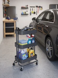 Three-tier RÅSKOG-style rolling garage cart holding car-care products, microfiber cloths, cleaning supplies, and a handheld vacuum.